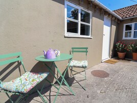 A small outdoor seating area with a table and two chairs, a window, and potted plants.