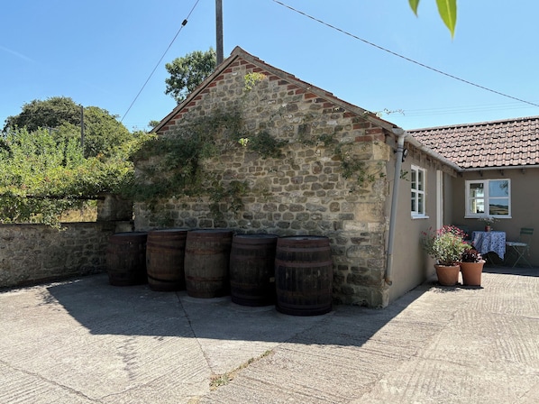 A stone building with a sloped roof, surrounded by six wooden barrels. - The Old Dairy (Warminster)