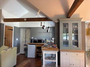 A compact kitchen with a refrigerator, stove, and hanging pots. There is a wooden bench and a cabinet with glass doors. - The Old Dairy (Warminster)