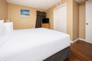 Una camera d'albergo con un letto grande, un televisore su una cassettiera in legno, un quadro appeso al muro e una porta chiusa.