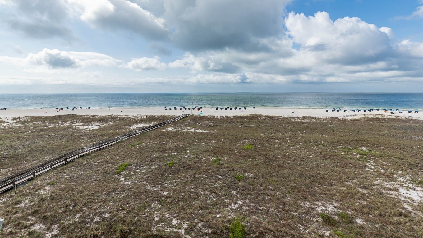 Een strand met een houten pier die naar het strand leidt, zandstrand en een bewolkte lucht.