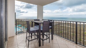 A balcony with a view of the sea, a pool, and a table with chairs. - Phoenix Vii 7502 1 Bedroom Condo (Orange Beach)