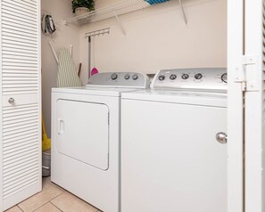 A laundry room with a front-loading washer and dryer, a drying rack, and a shelf above. - Phoenix Vii 7502 1 Bedroom Condo (Orange Beach)