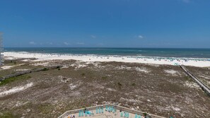 Uma praia com um calçadão de madeira, área arenosa com espreguiçadeiras e uma vista clara do oceano.