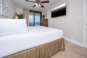 Une chambre d’hôtel avec un lit, un ventilateur de plafond, un téléviseur fixé au mur et une vue sur le balcon extérieur.