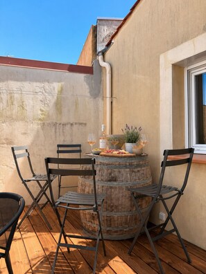 Eine Terrasse im Freien mit einem runden Holztisch, Metallstühlen und einem Blumentopf.
