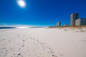A sandy beach with footprints leading towards the ocean and buildings in the background. - Phoenix Vii 7314 1 Bedroom Condo (Orange Beach)