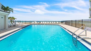 Una piscina rectangular amb aigua blava cristal·lina, envoltada per una tanca de metall negre, i una filera de gandules blanques al costat esquerre.