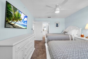 Ein Schlafzimmer mit zwei Betten, einem Deckenventilator, einem Strandbild und einer Tür zu einem anderen Raum.