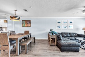 Ein modernes Wohnzimmer mit Essbereich, ausgestattet mit einem Holztisch, einer Ledersofa und einem Deckenventilator.