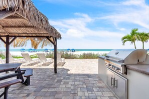 A beachside patio with a grill, lounge chairs, and a thatched roof structure. - 🌞Direct Beach Access🌴Heated Pool🐠Sunset Views☀Seagate 407 (Indian Shores)