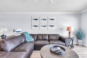A modern living room with a leather sectional sofa, a round coffee table, and six framed whale illustrations on the wall. - 🌞Direct Beach Access🌴Heated Pool🐠Sunset Views☀Seagate 407 (Indian Shores)