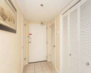 A hallway with a closed door, a tiled floor, and a wall-mounted light fixture. - Phoenix Vii 7214 1 Bedroom Condo (Orange Beach)