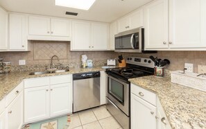 A kitchen with white cabinets, a granite countertop, a dishwasher, a stove, and a microwave. - Phoenix Vii 7214 1 Bedroom Condo (Orange Beach)