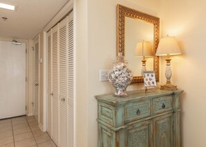 A hallway with a door, a mirror, a decorative cabinet, and a lamp. - Phoenix Vii 7214 1 Bedroom Condo (Orange Beach)