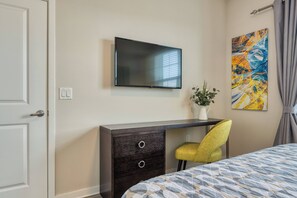 A hotel room with a bed, a desk with a chair, a flat-screen TV mounted on the wall, and a painting. - Vcr1-303 - 3BR Condo w Resort Access Near Parks (Orlando)