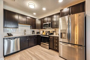 A modern kitchen with dark cabinets, stainless steel appliances, and a wooden floor. - Vcr1-303 - 3BR Condo w Resort Access Near Parks (Orlando)