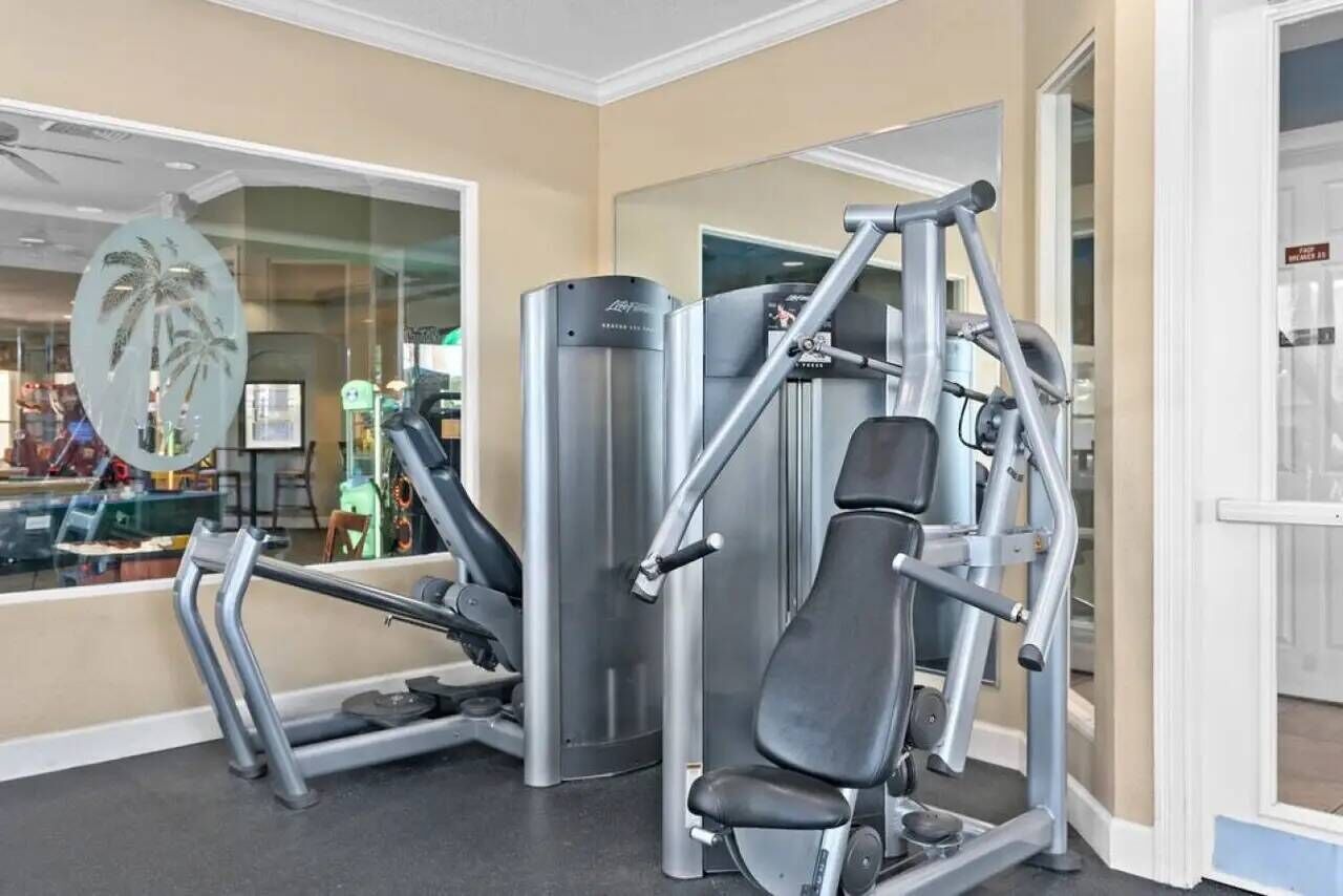 A gym with exercise equipment, a glass wall with a palm tree decoration, and a door leading to another room.