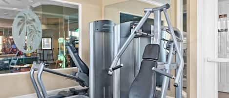 Un gimnasio con equipo de ejercicio, un muro de cristal decorado con una palmera y una puerta que da a otra habitación.