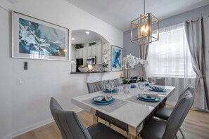 A modern dining area with a white table set for six, grey upholstered chairs, and a chandelier. - Wh7754 - 6BR House With Pool Near Disney (Kissimmee)
