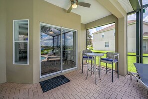 A covered patio with a table and chairs, a ceiling fan, and a view of a swimming pool and greenery. - Wh2584 - 6BR House With Pool Near Disney Parks (Kissimmee)