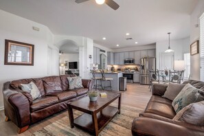 A spacious living room with a brown leather sofa, a wooden coffee table, and a kitchen area in the background. - Wh2584 - 6BR House With Pool Near Disney Parks (Kissimmee)