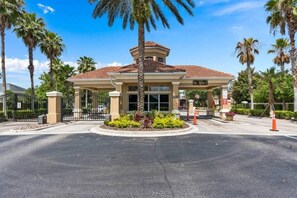 A hotel entrance with a covered area, palm trees, and a gated driveway. - Wh2584 - 6BR House With Pool Near Disney Parks (Kissimmee)