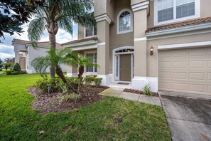 A two-story residential building with a beige exterior, a front entrance with a door and window, and a garage door. - Wh2584 - 6BR House With Pool Near Disney Parks (Kissimmee)
