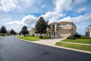 A residential street with houses, a clear sky, and a well-maintained lawn. - Wh2584 - 6BR House With Pool Near Disney Parks (Kissimmee)
