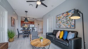 Un salon moderne avec un canapé en cuir noir, une table basse en bois et un coin repas agrémenté d’un lustre.