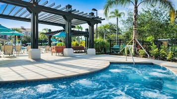 A pool area with a hot tub, lounge chairs, and umbrellas.