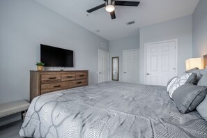 A bedroom with a bed, a TV on a dresser, a ceiling fan, and two doors. - Is1-208 - 3BR Condo Near Disney With Lake View (Orlando)