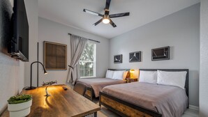 Une chambre moderne avec deux lits, un bureau, un ventilateur de plafond et une télévision.