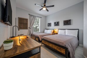 Ein modernes Schlafzimmer mit zwei Betten, einem Schreibtisch, einem Deckenventilator und einem Fernseher.