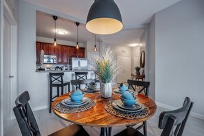 A dining area with a round wooden table, black chairs, and blue dinnerware. A black pendant light hangs above the table. - Is1-208 - 3BR Condo Near Disney With Lake View (Orlando)