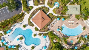 Luchtbeeld van een resort met meerdere zwembaden, ligbedden en een centraal gebouw met een rood dak.
