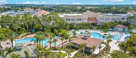 Un resort con varias piscinas, palmeras y un edificio grande con techo de tejas rojas.