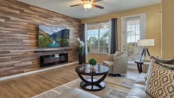 A living room with a wooden wall, a flat-screen TV, a fireplace, a round coffee table, a sofa, and a window with curtains.