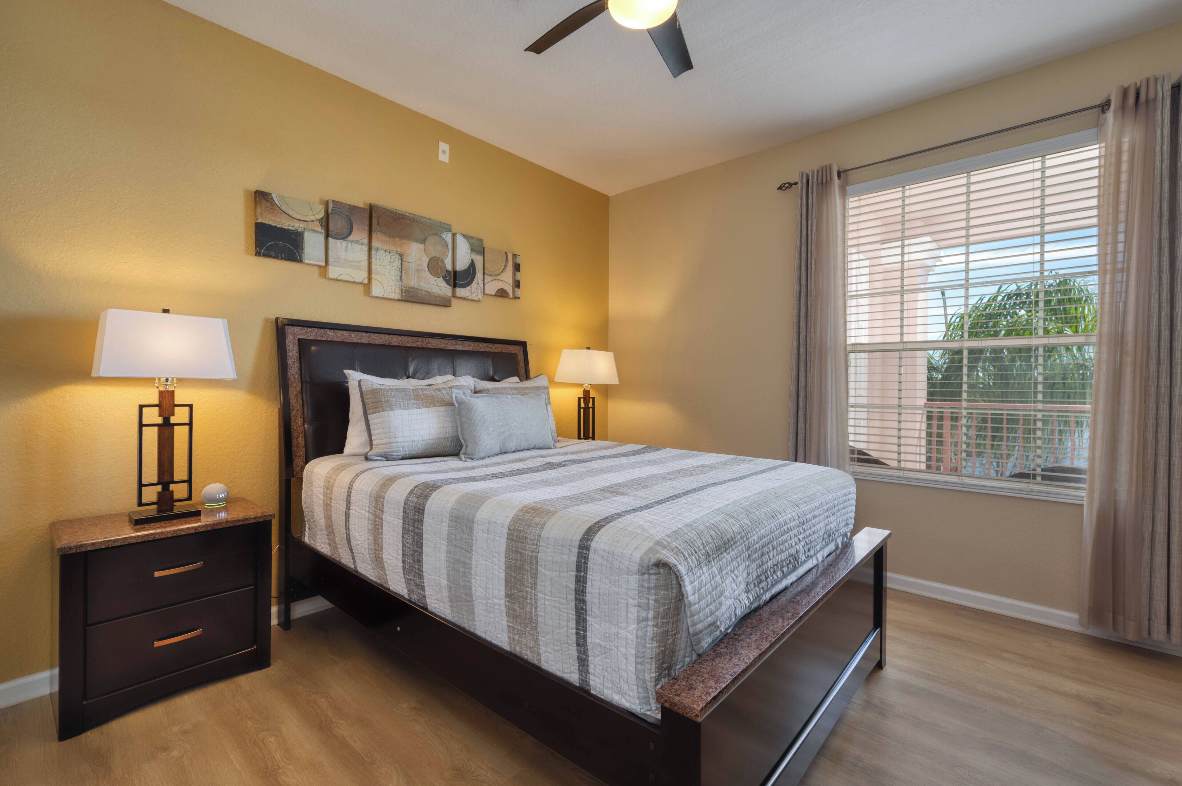 A bedroom with a bed, two bedside tables, a ceiling fan, and a window with curtains.