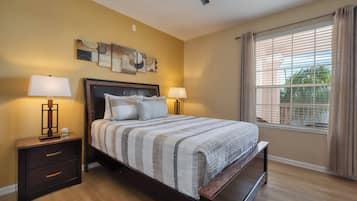 A bedroom with a bed, two bedside tables, a ceiling fan, and a window with curtains.