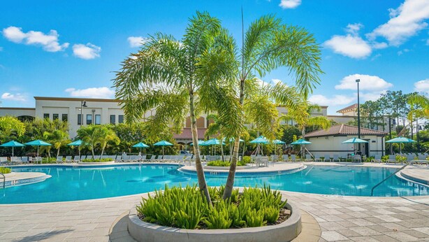 A pool area with lounge chairs and umbrellas, surrounded by palm trees and a building in the background. - Th155 - 3BR House Near Disney, Sleeps 8 Guests (Orlando)