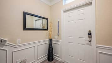 Un pasillo con una puerta blanca, un espejo enmarcado y un jarrón negro con ramas decorativas.