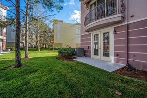 A residential building with a balcony, a well-maintained lawn, and a neighboring building. - Th60 - 3BR House Near Disney With Pool Access (Orlando)