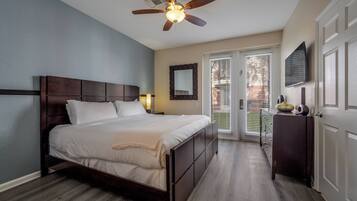 A bedroom with a wooden bed, a ceiling fan, a television, and a door leading to a balcony.