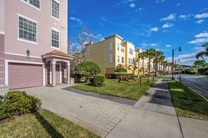 A row of townhouses with a paved driveway, a well-maintained lawn, and a clear blue sky. - Th60 - 3BR House Near Disney With Pool Access (Orlando)