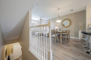 Uma sala de estar moderna com área de jantar, escada e ventilador de teto.