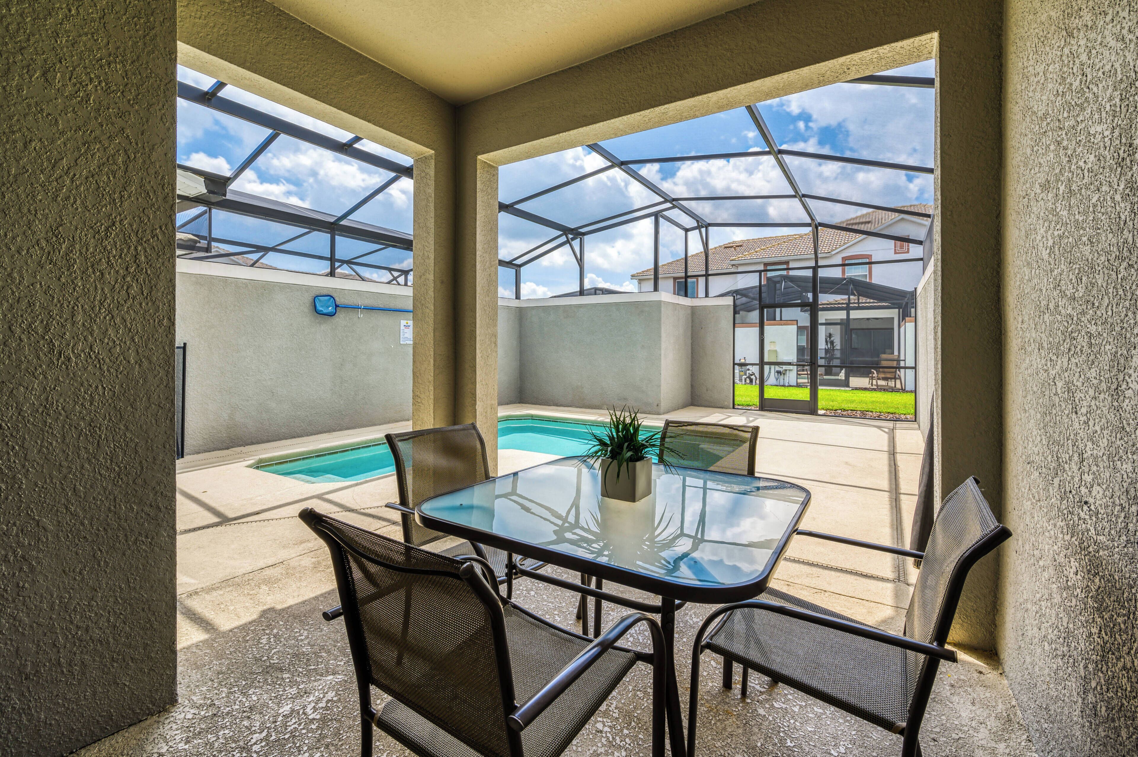 A glass-enclosed patio with a pool, outdoor furniture, and a view of a residential area.