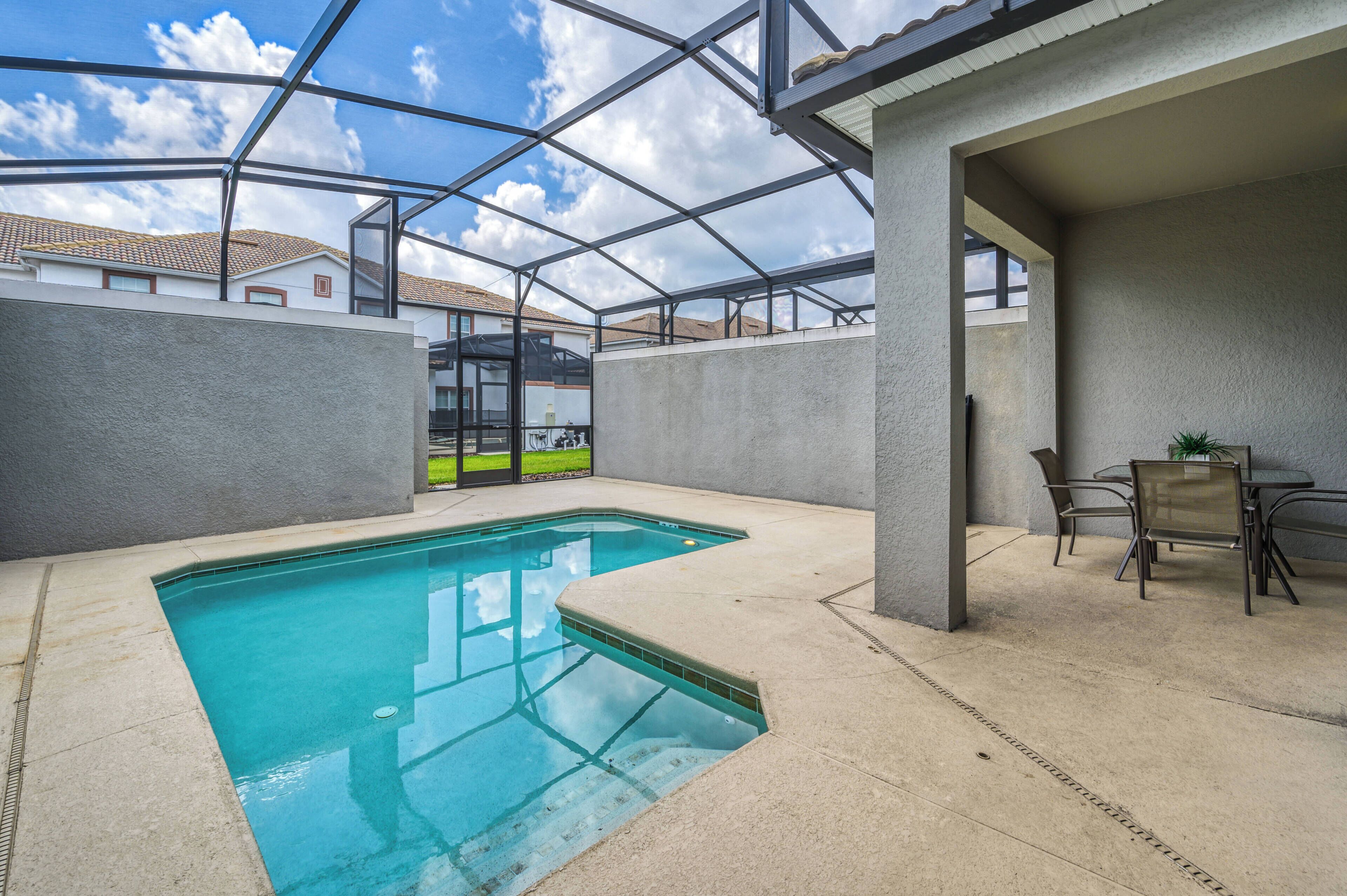 Una piscina con techo de vidrio, un área de patio con sillas y vistas a casas vecinas.