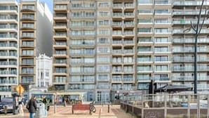 Een meerlaags woongebouw met balkons, een verharde begane grond en een zichtbare winkelruimte.