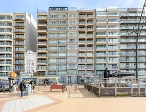 A multi-story residential building with balconies, a paved ground floor, and a visible storefront. - Blankenberge Apartment for 4 (Blankenberge)